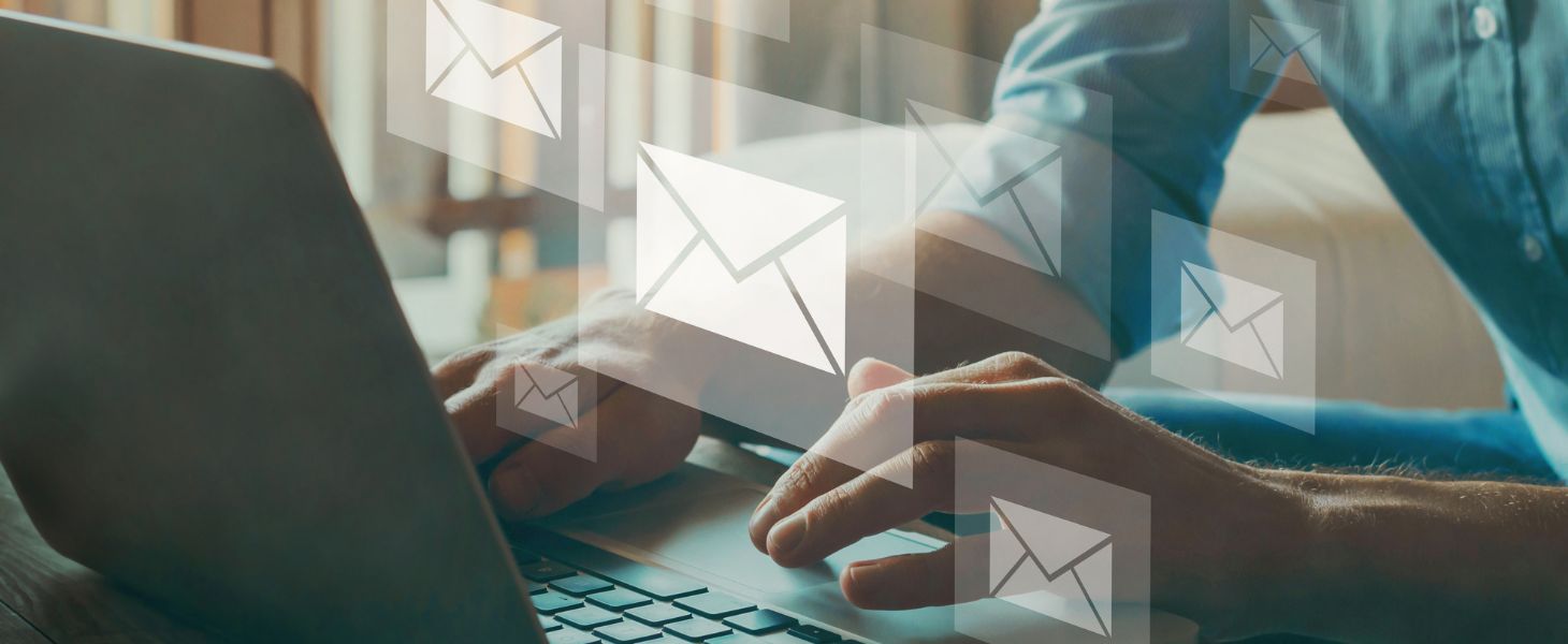 Person tippt auf einem Laptop, darüber eingeblendete Briefumschlag-Symbole – symbolisch für digitale Kommunikation, E-Mail-Verkehr und automatisierte Nachrichtenprozesse